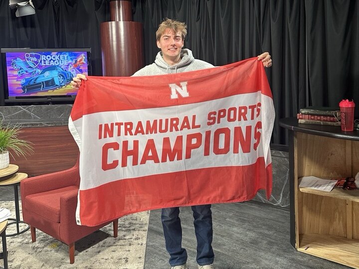 Person holding a red and white "Intramural Sports Champions" banner in a studio setting.