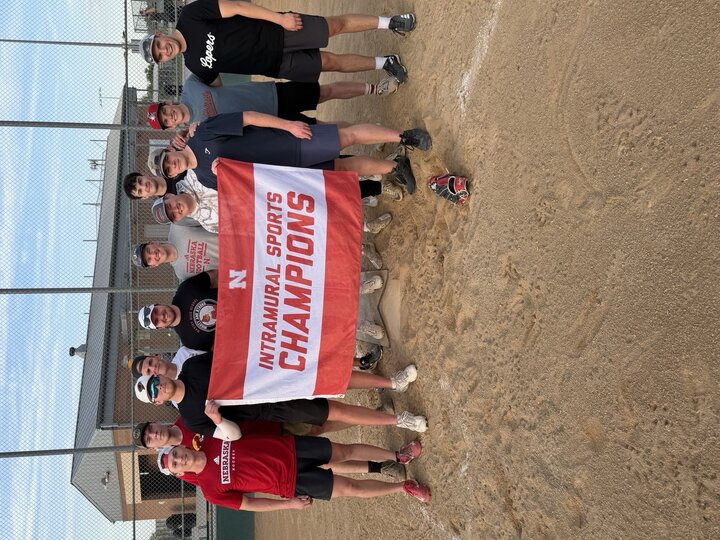 Men standing in a dirt field holding a red-and-white "Intramural Sports Champions" banner.