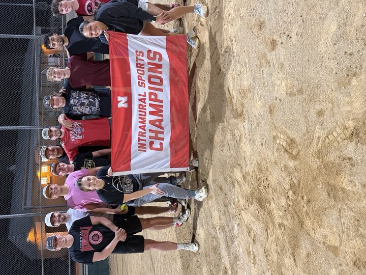 Team posing with an "Intramural Sports Champions" banner on a sandy field at night.