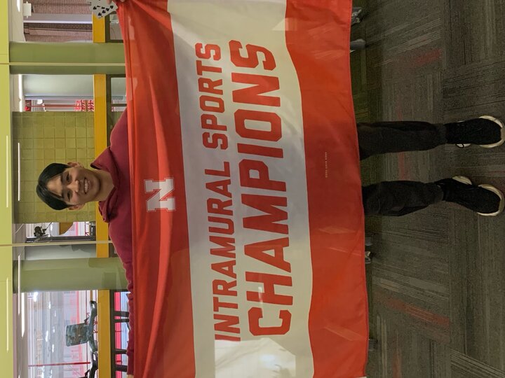 Person holding a red and white banner that reads "Intramural Sports Champions" indoors.