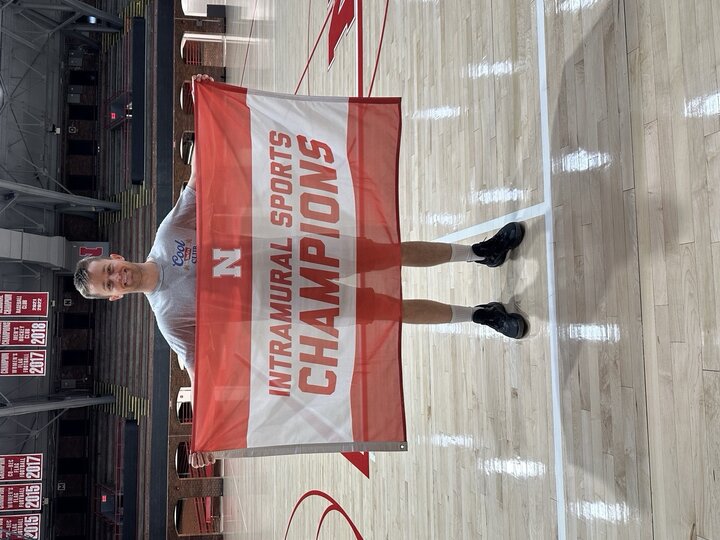 Man holding "Intramural Sports Champions" banner on a basketball court.