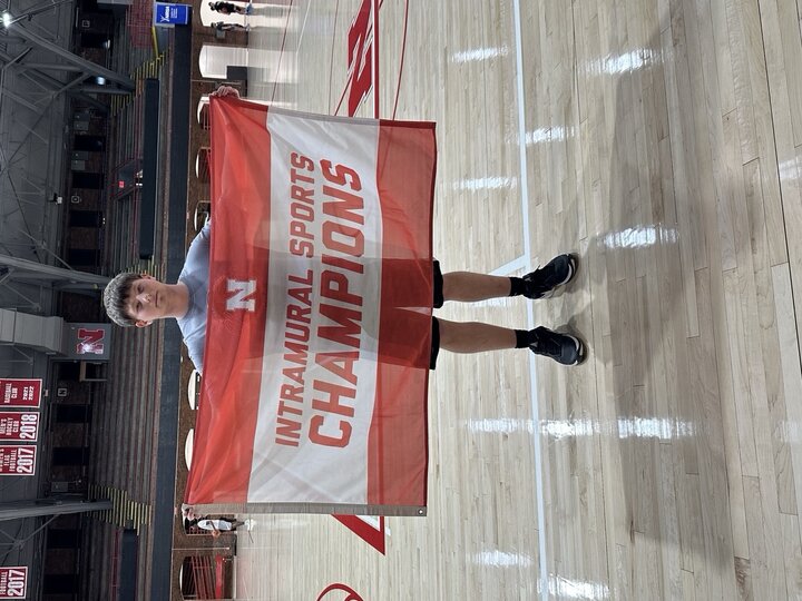 Person holding a red and white "Intramural Sports Champions" banner on a basketball court.