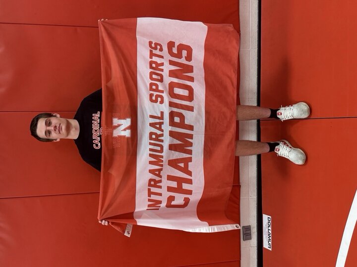Person holds red and white "Intramural Sports Champions" banner against matching red wall.