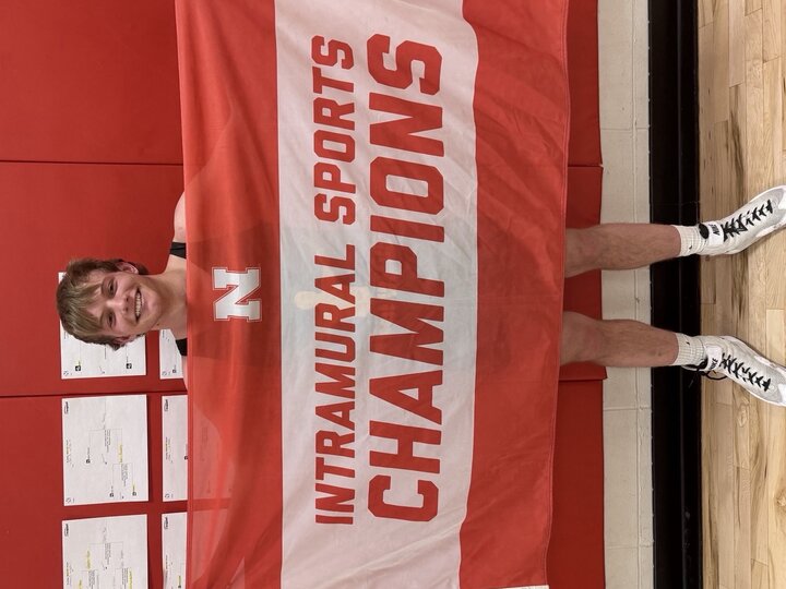 Person holding a red and white banner reading "Intramural Sports Champions" against a red wall.