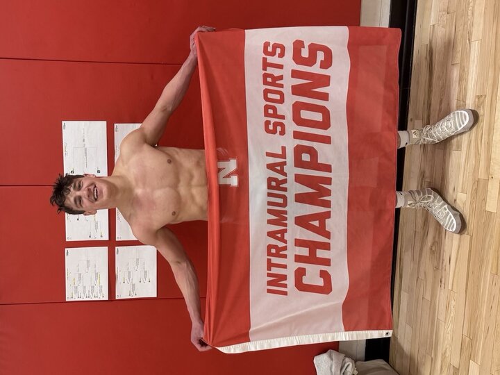 Shirtless person holding a red and white "Intramural Sports Champions" banner in a gym.