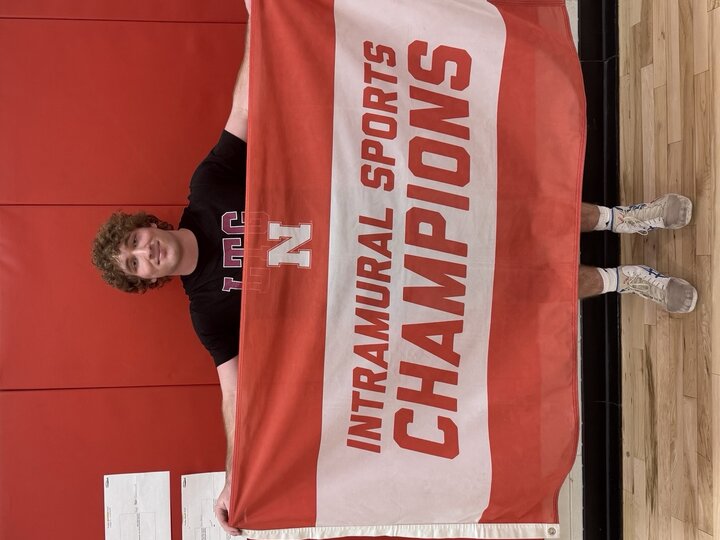Man holding a red and white "Intramural Sports Champions" banner in front of a red wall.