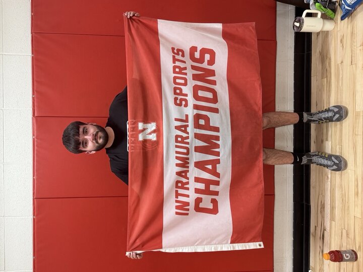 Man holding a red and white "Intramural Sports Champions" banner, standing against a red wall.