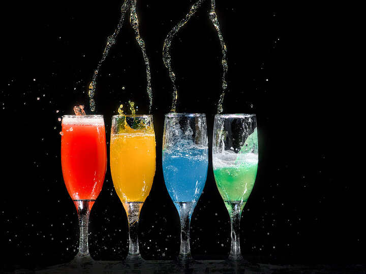 Long stem alcohol glasses sit in front of a black background with bright colored drinks inside