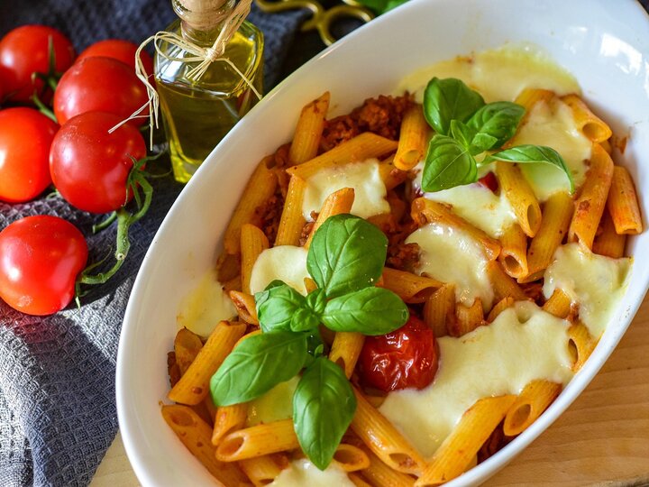 chicken feta pasta served in a white bowl next to cherry tomatoes