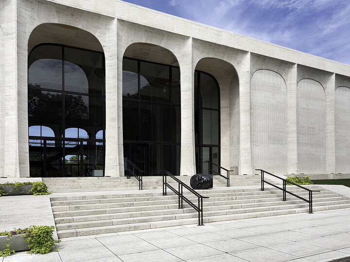 Modern building with large arched windows, steps, and railings, set against a blue sky 