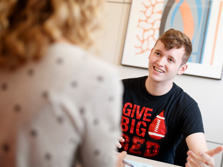 Two people in conversation; one wears a black shirt with red text, blurred faces for privacy.