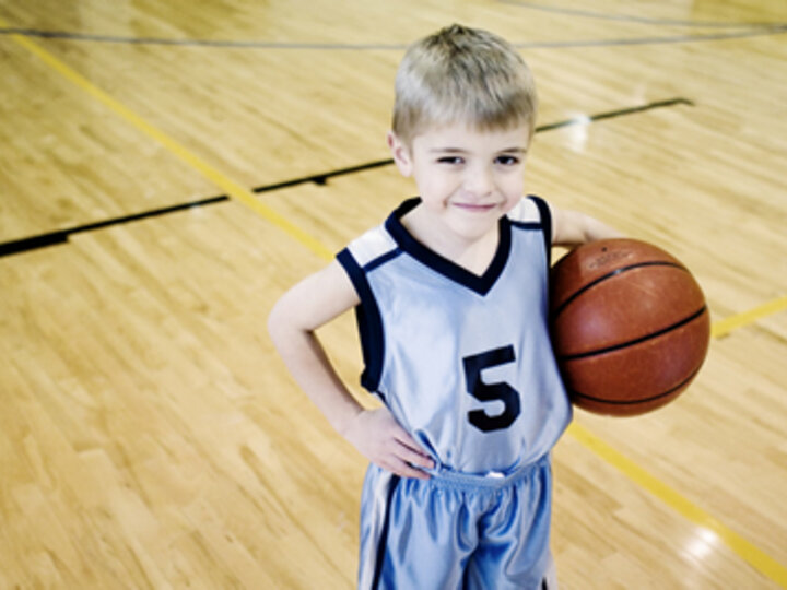 Child holds a basketball under their arm on a basketball court