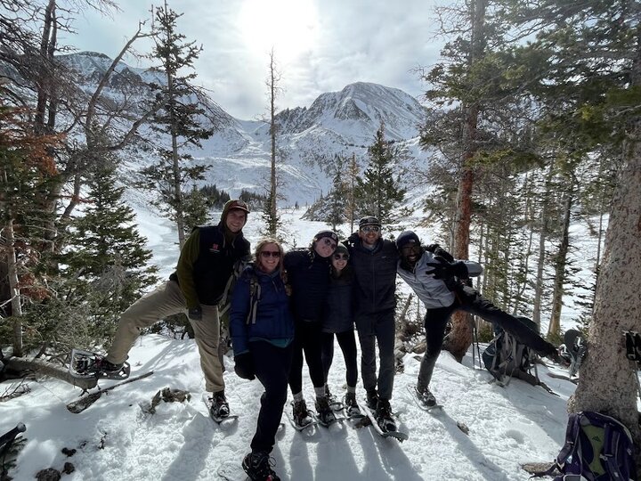A group of students stands in the mountains with snowshoes