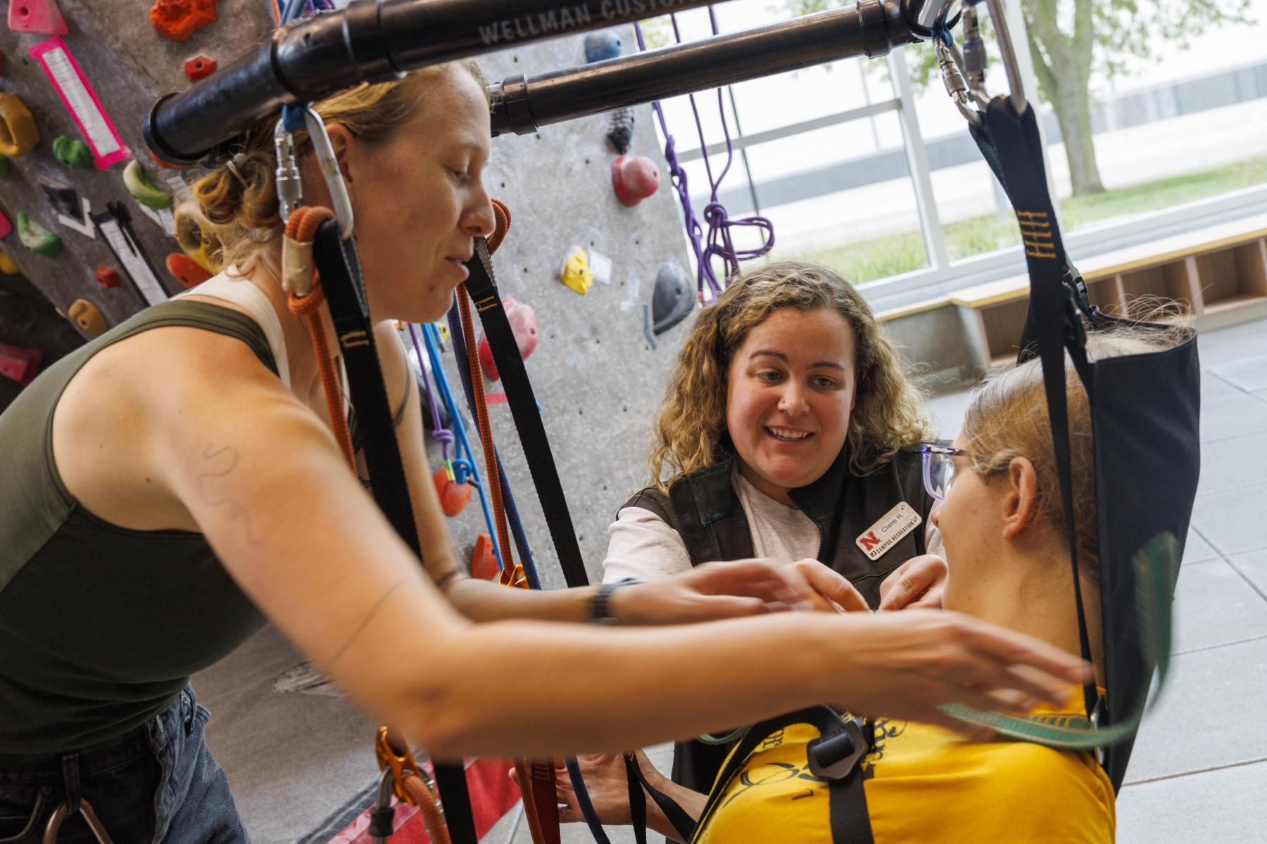 Outdoor Adventures staff strap a climber into the accessibility climbing harness in the Outdoor Adventures Center