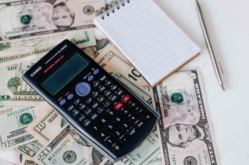 Calculator, notepad, pen, and money on a white surface