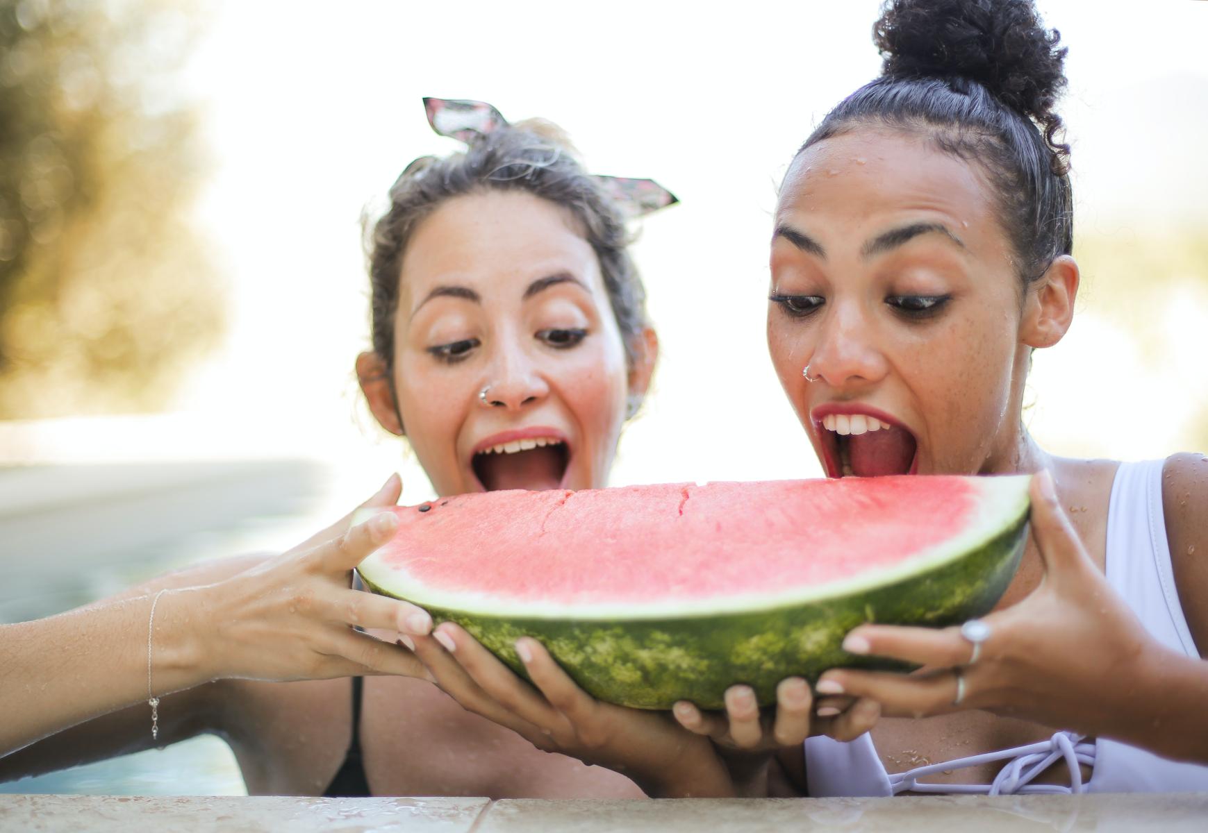 Individuals taking a bite out of a slice of watermelon.