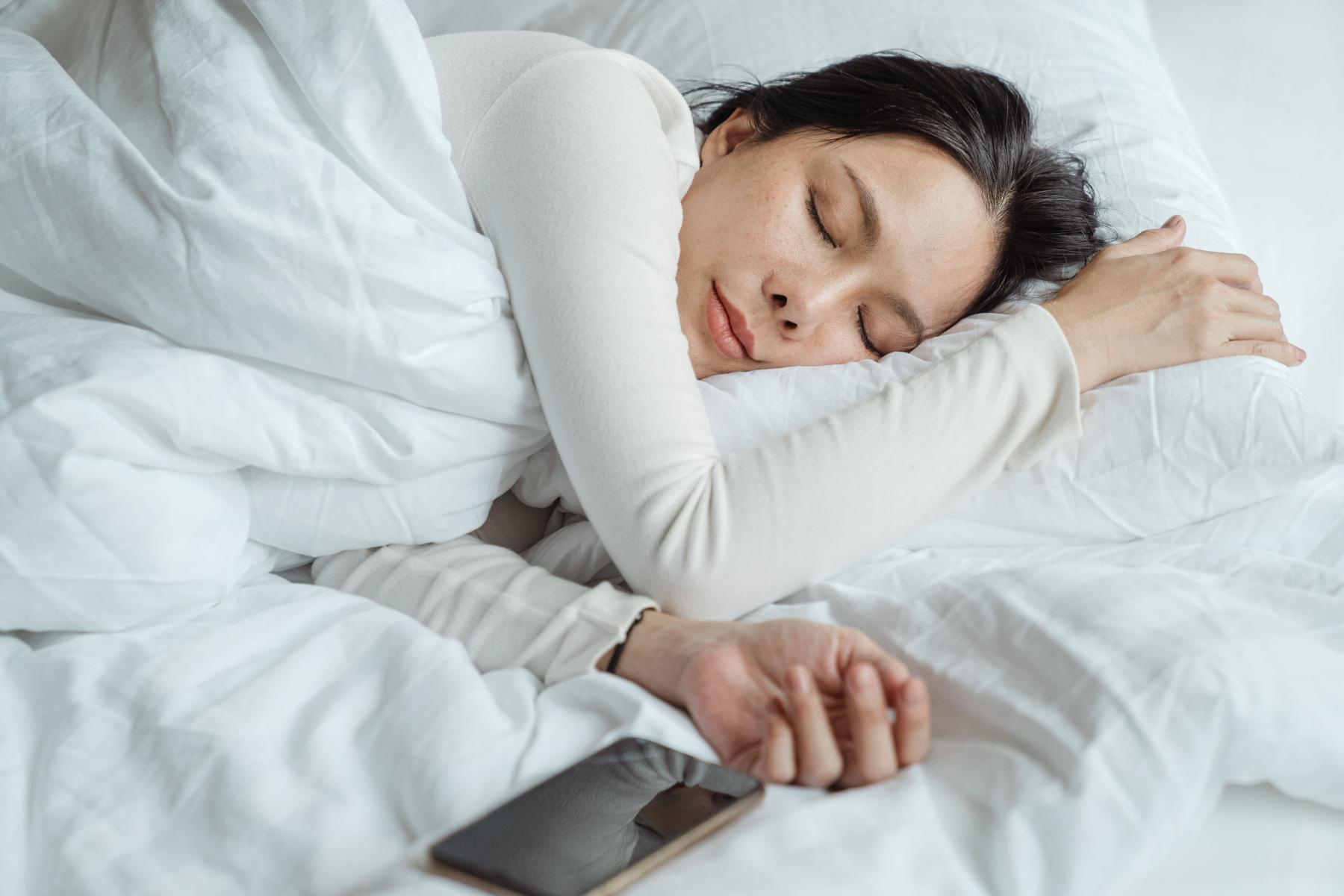 Woman sleeping in white bedding with a phone next to her